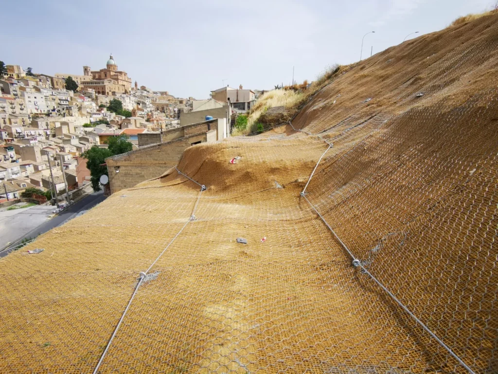 Versante rivestito con geostuoia e rete metallica, sullo sfondo Piazza Armerina